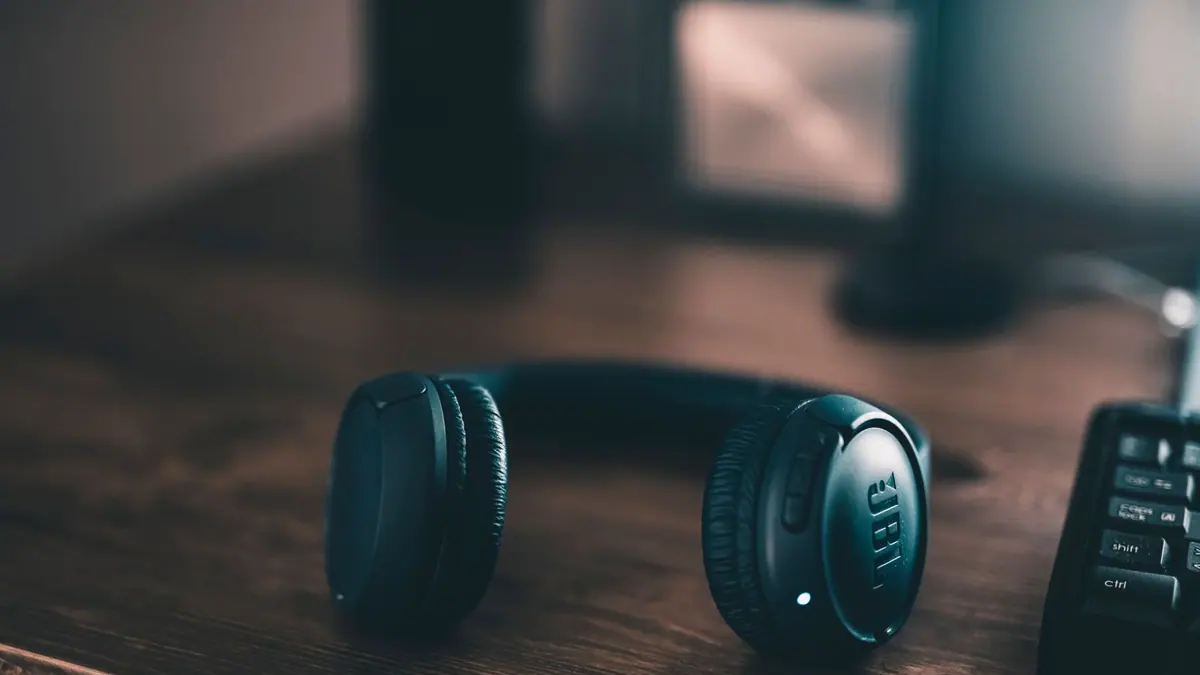 A pair of over-ear headphones resting on a wooden desk beside a notebook
