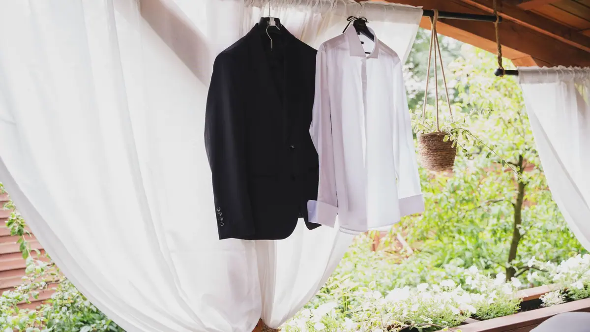 A white shirt hanging on a wooden hanger against a plain wall