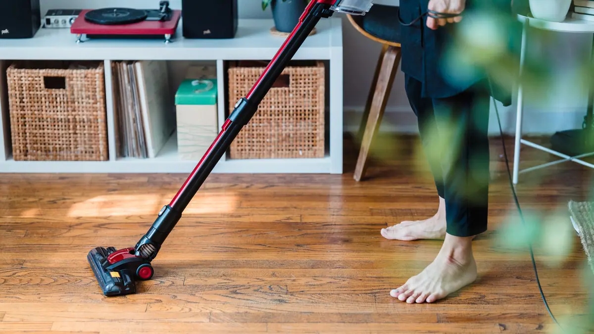 A cordless stick vacuum standing beside a sofa